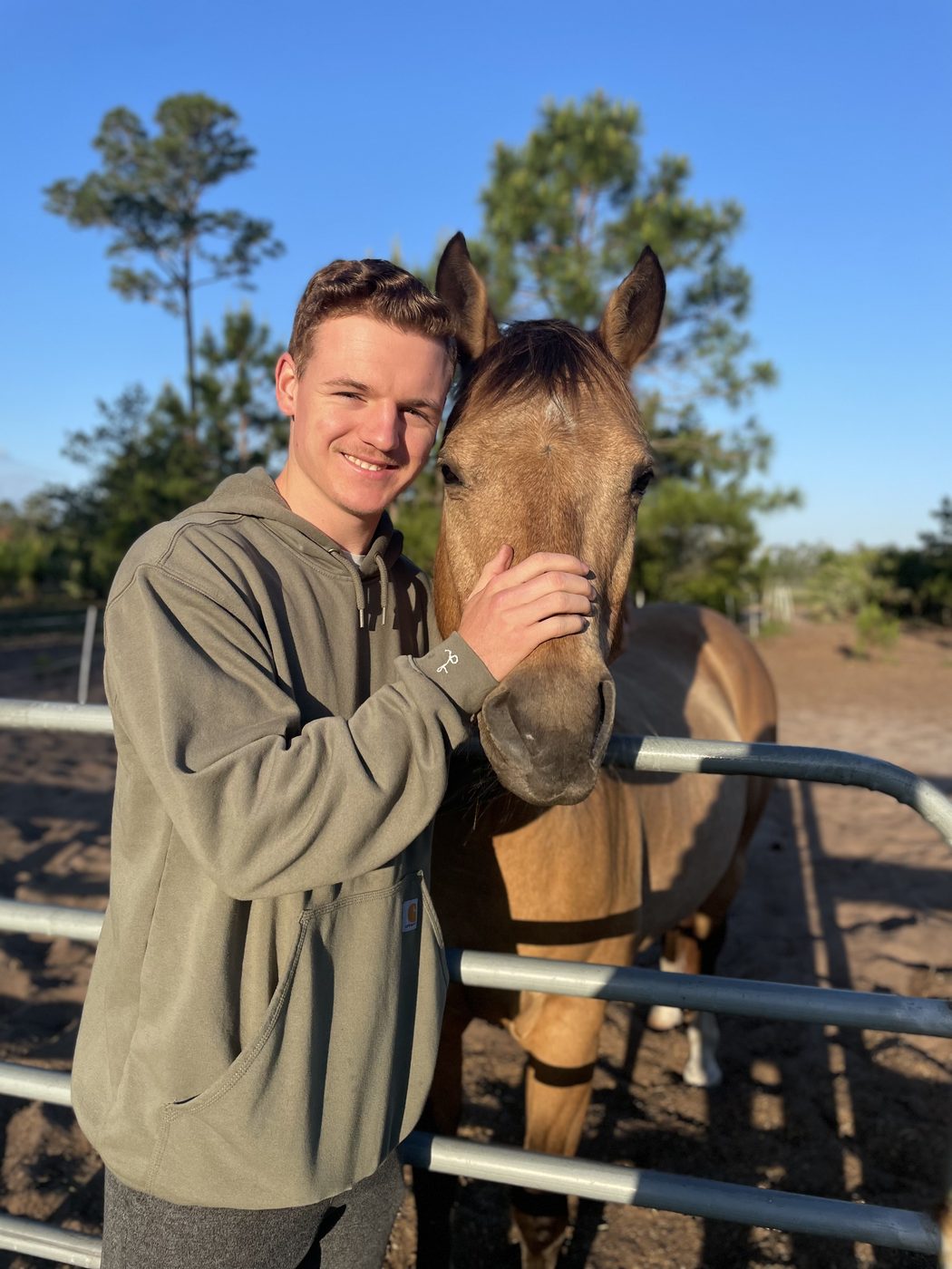 A young man pets a buckskin horse at a pipe gate at The Refuge